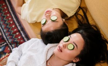 Two women enjoying a relaxing spa day with cucumber masks in a cozy home setting.